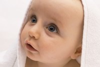Baby schaut neugierig unter einem wei&szlig;en Handtuch hervor.