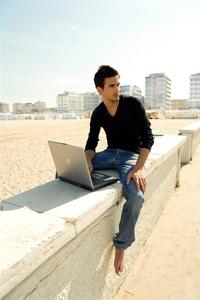 Mann arbeitet mit Laptop am Strand
